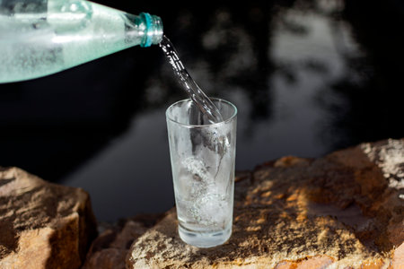 cold mineral water from a bottle is poured into a glass in nature on a dark background. High quality photoの写真素材