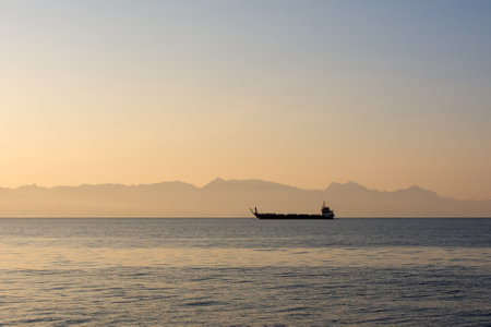 a cargo barge ferry floats at dawn on the sea against the backdrop of mountains in the fog, cargo and passenger transportationの写真素材