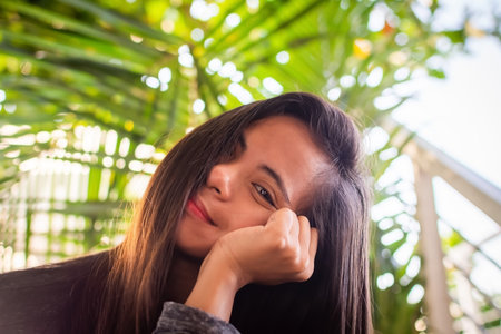 portrait of a beautiful young Filipina woman against a background of palm leaves in the rays of the sunの写真素材