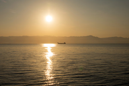 a ship floats at dawn on the sea against the backdrop of mountains and the rising sunの写真素材
