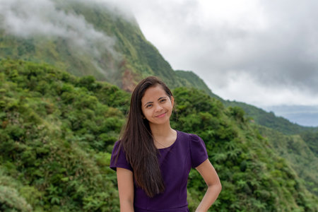 Portrait of a beautiful young Filipina woman against the backdrop of tropical mountains covered with cloudsの写真素材