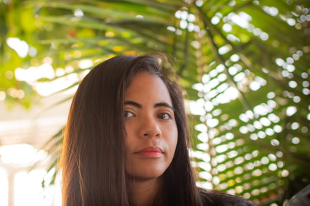 portrait of a beautiful Filipina woman against a background of palm leaves in the rays of the sun