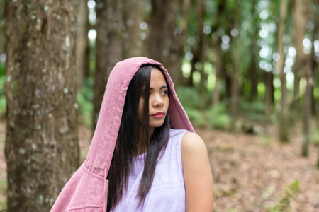 young filipino woman in the forest wearing a pink cape with a hood, walking outdoorsの写真素材