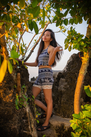 young beautiful asian woman in a bathing suit against the background of rocks and tropical trees.の写真素材