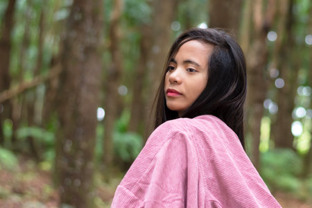 young filipino woman in the forest wearing a pink cape with a hood, walking outdoors.の写真素材