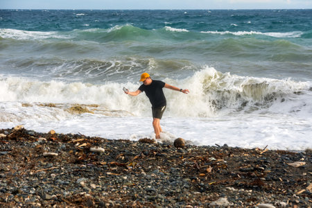 a man with a smartphone in his hand runs away from big waves on the sea coast.の写真素材