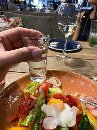 shot glass in hand in a restaurant on a background of appetizers and vegetable salad.の写真素材