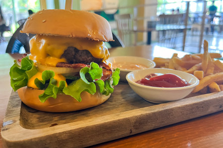 big juicy burger and french fries with sauces on wooden tray on table against cafe backgroundの写真素材