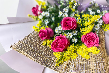 delicate bouquet with roses in purple paper complemented by small yellow flowersの写真素材