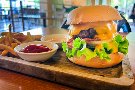 big juicy burger and french fries with sauces on wooden tray on table against cafe backgroundの写真素材