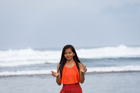 Smiling young beautiful asian woman making heart sign with fingers by the seaの写真素材