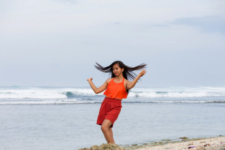Joyful asian young woman dancing on ocean shoreの写真素材