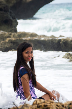 Woman smiling as ocean wave crashes dramatically behind herの写真素材