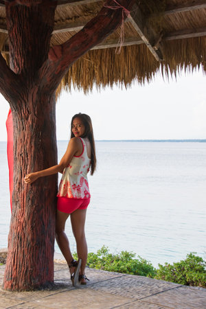 Playful young woman posing near tree in hut by seaの写真素材