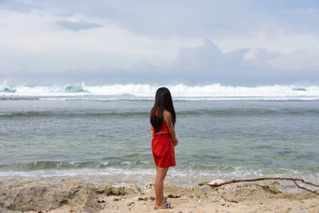 A young lonely woman stands on the shore of a stormy sea and looks into the distance at the wavesの写真素材