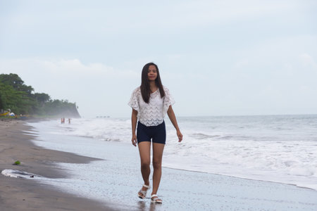 young woman walking alone on the beach near the sea wavesの写真素材