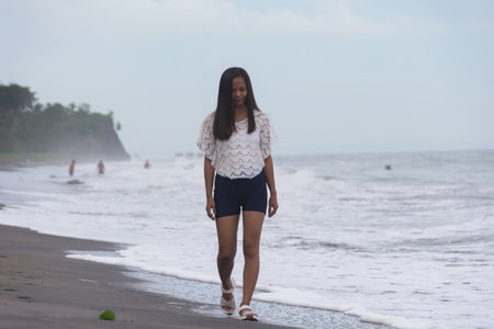 young woman walking alone on the beach near the sea wavesの写真素材