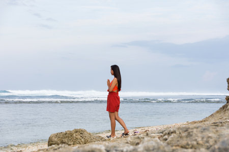 A young woman stands in front of the sea with her hands folded in prayerの写真素材