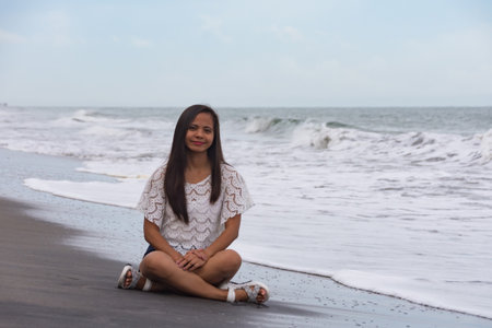 young woman sitting on sand beach near wavesの写真素材