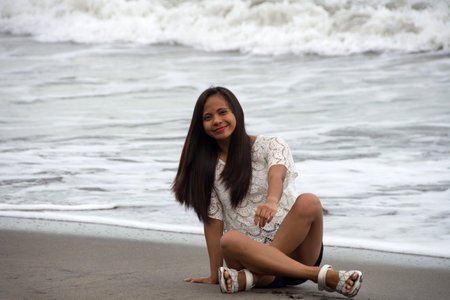 young asian woman smiling sitting on the coast of tropical wavy seaの写真素材