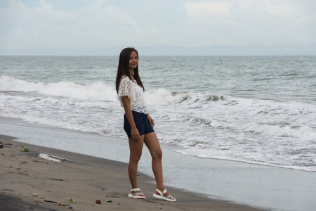 Confident woman standing on beach near sea wavesの写真素材