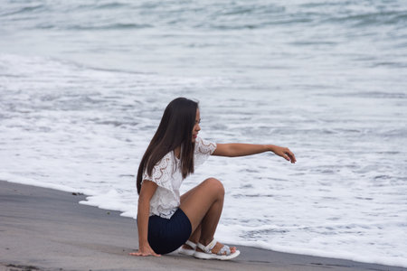 young asian woman smiling, sitting on sandy beach near seaの写真素材