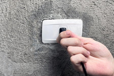 A smoking electrical outlet, a hand pulling the plug out of a burning outletの写真素材