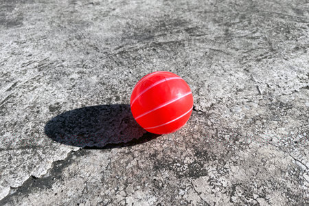 red plastic toy ball with white stripes on concrete ground with shadow