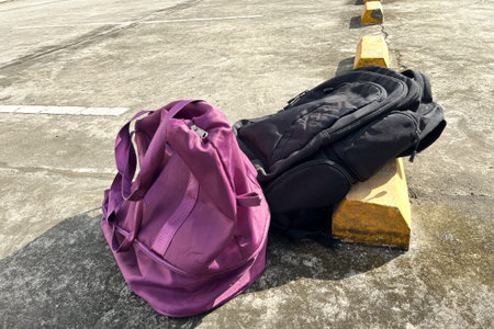 purple duffel bag and black backpack on concrete pavement in outdoor parking lot