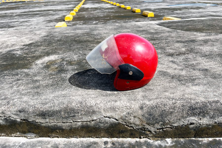 red open face motorcycle helmet on concrete pavement near row of yellow parking wheel stops