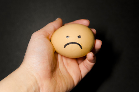Sad fresh chicken egg in the hand of a person. Sad smile on the face. Organic food close up. Stay...
