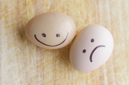 Sad and happy fresh chicken eggs on the wooden table. Sad and happybsmile on the face. Organic food close up. Stay healthy. The contrast of happiness and sadness concept.の写真素材