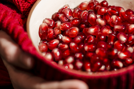 Peeled pomegranate in the bowl covered with red sweather. Background is black. Fresh organic food in the hands. Stay healthy concept.の写真素材