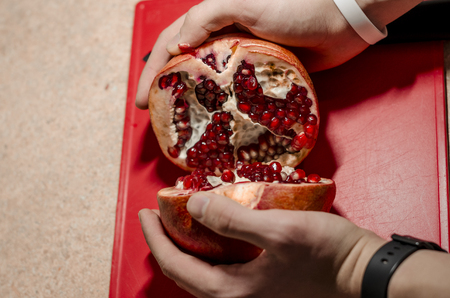 Human hands peeling fruit. Fresh pomegranate seeds on the red cutting board. The background is white. Ripe organic food close up. Stay healthy concept.の写真素材