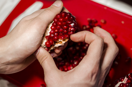 Human hands making a heart of fresh pomegranate pices on the red cutting board. The background is red. Ripe organic food close up. Stay healthy concept. Broken symbol of love.の写真素材