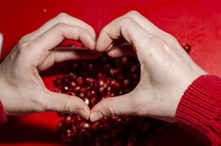 Human hands making a heart in front of fresh pomegranate seeds on the red cutting board. The background is red. Ripe organic food close up. Stay healthy concept.の写真素材