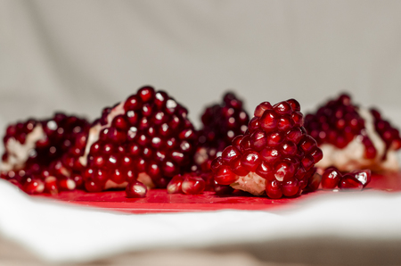 Fresh pomegranate seeds on the red cutting board from the side view. The background is white. Ripe organic food close up. Stay healthy concept.の写真素材
