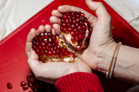 Human hands making a heart of fresh pomegranate pices on the red cutting board. The background is red. Ripe organic food close up. Stay healthy concept. Broken symbol of love.の写真素材