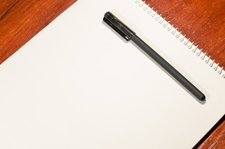 A blank page of an open notebook is on the wooden table with a black pen. Place for writing anything you want. Business and education concept. Texture background of a white sheet of paper.の写真素材