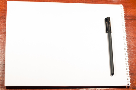 A blank page of an open notebook is on the wooden table with a black pen. Place for writing anything you want. Business and education concept. Texture background of a white sheet of paper.の写真素材
