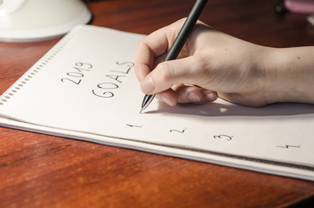Writing the list of goals for 2019 year concept. Human hand with a black pan and blank page of notebook. Education and business.の写真素材