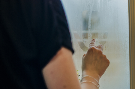 Woman's hand drawing a happy face on the foggy window. Water droplets condensation background of dew on glass, humidity and foggy close up view. Outside the house. Be happy even in bad raining weather concept.の写真素材