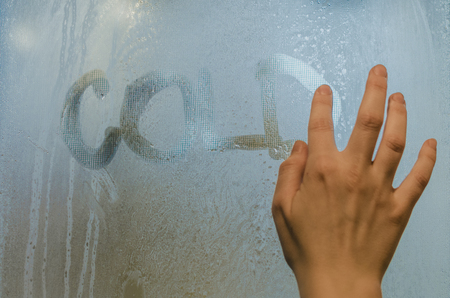 Human hand writing word 'Cold' on the foggy window. Water droplets condensation background of dew on glass, humidity and foggy close up view. Outside the house, bad raining weather concept.の写真素材