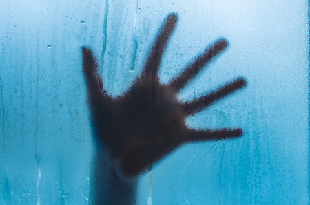 A hand on the sweaty fogged window. Water droplets condensation background of dew on glass, humidity and foggy close up view. Outside the house, bad raining weather.の写真素材