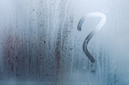 Drawn question mark on the foggy window. Water droplets condensation background of dew on glass, humidity and foggy close up view. Outside the house, bad raining weather.の写真素材