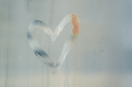 A heart is drawn on the sweaty foggy window. Water droplets condensation background of dew on glass, symbol of love close up view. Be happy and love even in bad raining weather outside concept.の写真素材