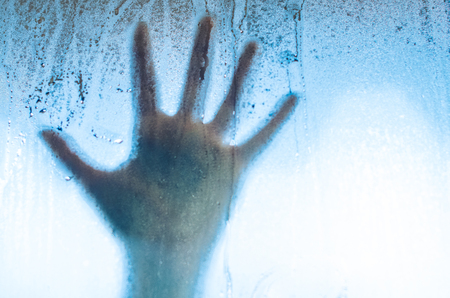 A hand on the sweaty fogged window. Water droplets condensation background of dew on glass, humidity and foggy close up view. Outside the house, bad raining weather.の写真素材