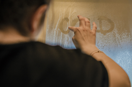 Human hand writing word 'Cold' on the foggy window. Water droplets condensation background of dew on glass, humidity and foggy close up view. Outside the house, bad raining weather.の写真素材