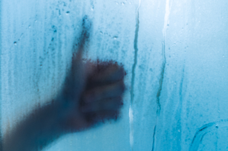 Human hand showing like outside the foggy window. Water droplets condensation background of dew on glass, humidity and foggy close up view. Outside the house, bad raining weather.の写真素材