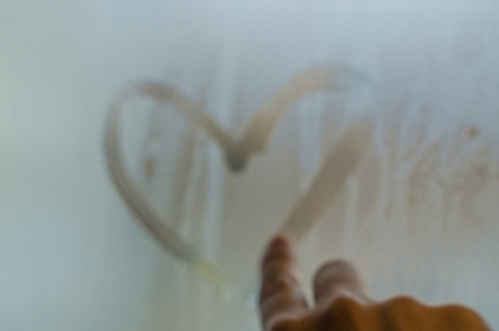 Woman hand drawing a heart on the sweaty foggy window. Water droplets condensation background of dew on glass, symbol of love close up. Be happy and love even in bad raining weather outside concept.の写真素材